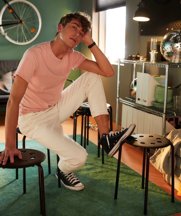 A student sitting on and resting his feet on a black stool.