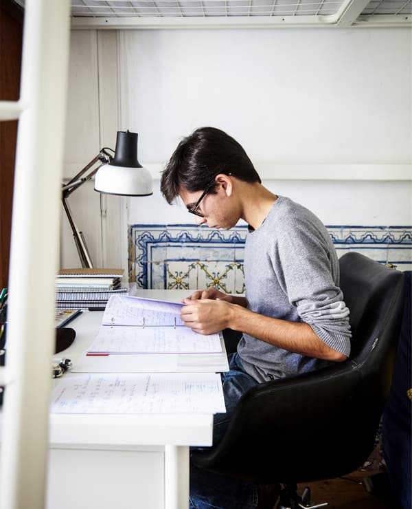 A student works at his bedroom desk. Old and new blend together with the modern white desk and historic wall tiles.