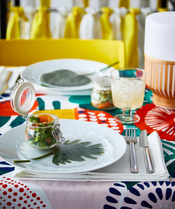 A summer party table setting with a salad served inside a clear glass IKEA KORKEN jar.