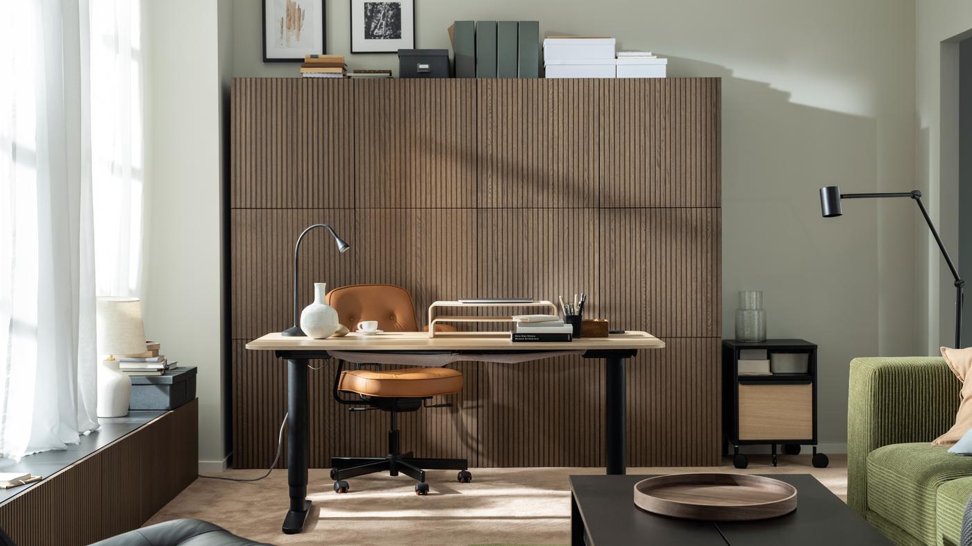 A sunlit workspace formed by a BEKANT sit-stand desk, an ALEFJÄLL office chair and a wall of wood-front BESTÅ cabinets.