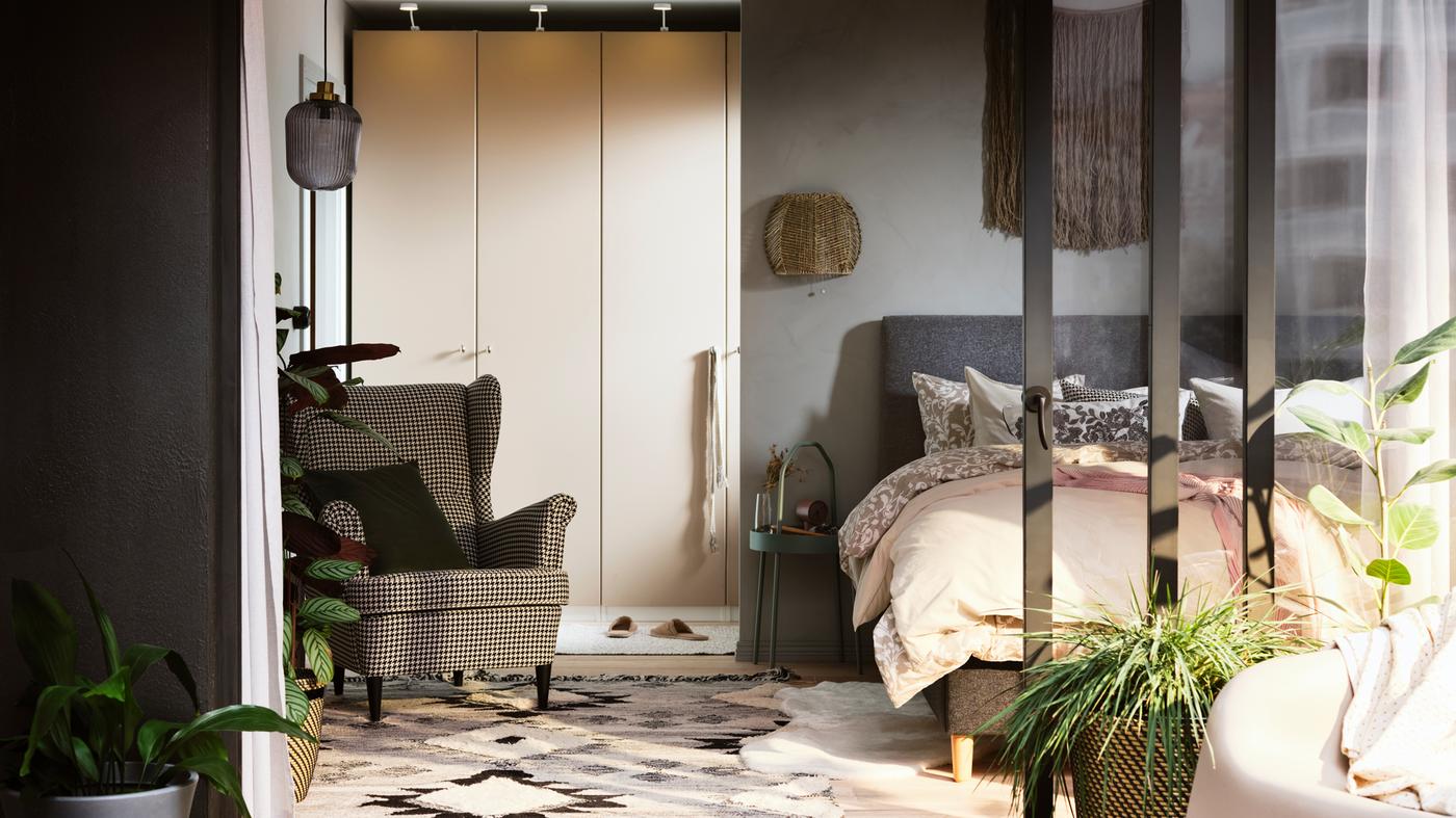 A sunny bedroom with a PAX/REINSVOLL wardrobe combination by an IDANÄS bed covered in a mix of floral and plain bed linen.