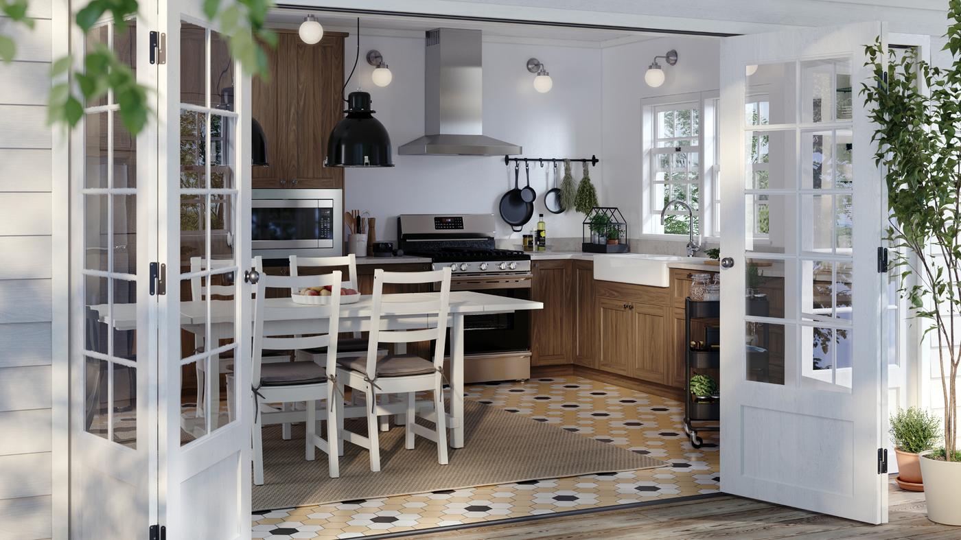 A sunny kitchen with walnut-effect ENKÖPING doors on the cabinets and a white table with some chairs around it.