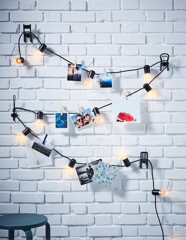 A SVARTRÅ LED lighting chain against a white brick wall, decorated with photos.