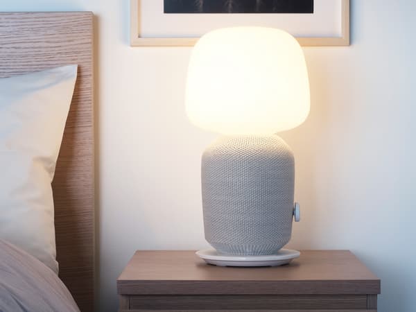 A SYMFONISK table lamp with WiFi speaker in white/grey placed on a bedside table.
