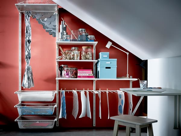 A table, chair and large shelving unit stocked with crafting supplies sit beneath a sloped ceiling.