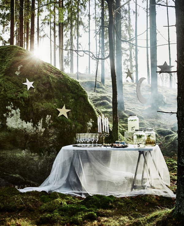 A table for mingle drinks at a forest wedding with a lace-like curtain tablecloth and hanging star decorations