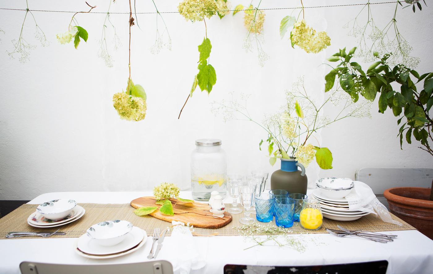 A table setting with patterned crockery, glasses and a vase of flowers, with flowers hanging above.