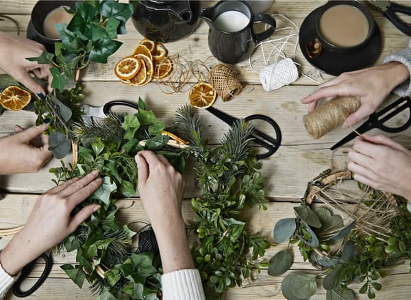 A table with three pairs of hands making festive wreaths.