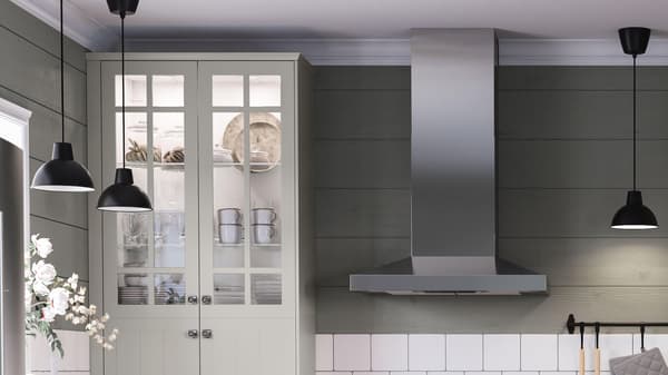 A tall beige cabinet next to a stainless range hood and black pendant lamps hanging from the ceiling.