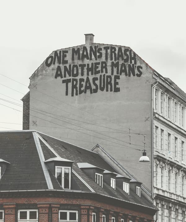 A tall, old building with graffiti on the side reading ‘one man’s trash another man’s treasure’