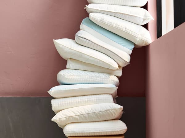 A tall stack of white and light blue pillows leans against a pink and gray wall, creating a cozy arrangement.