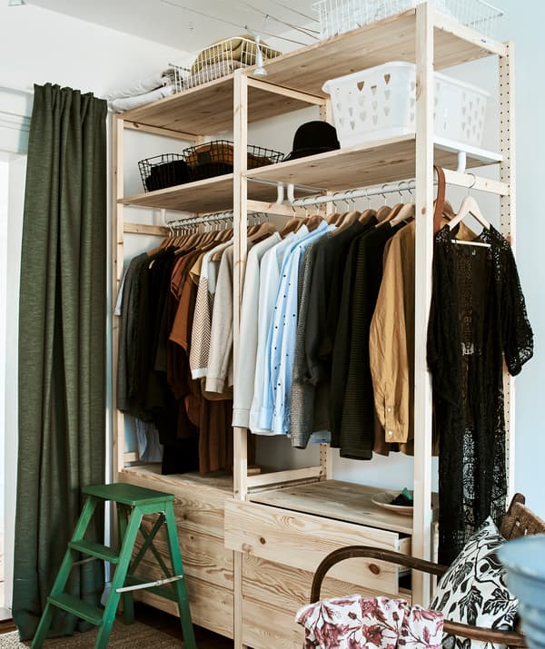 A tall wood clothes storage unit with drawers, a clothes rail and shelves for boxes and a green step stool in the corner.