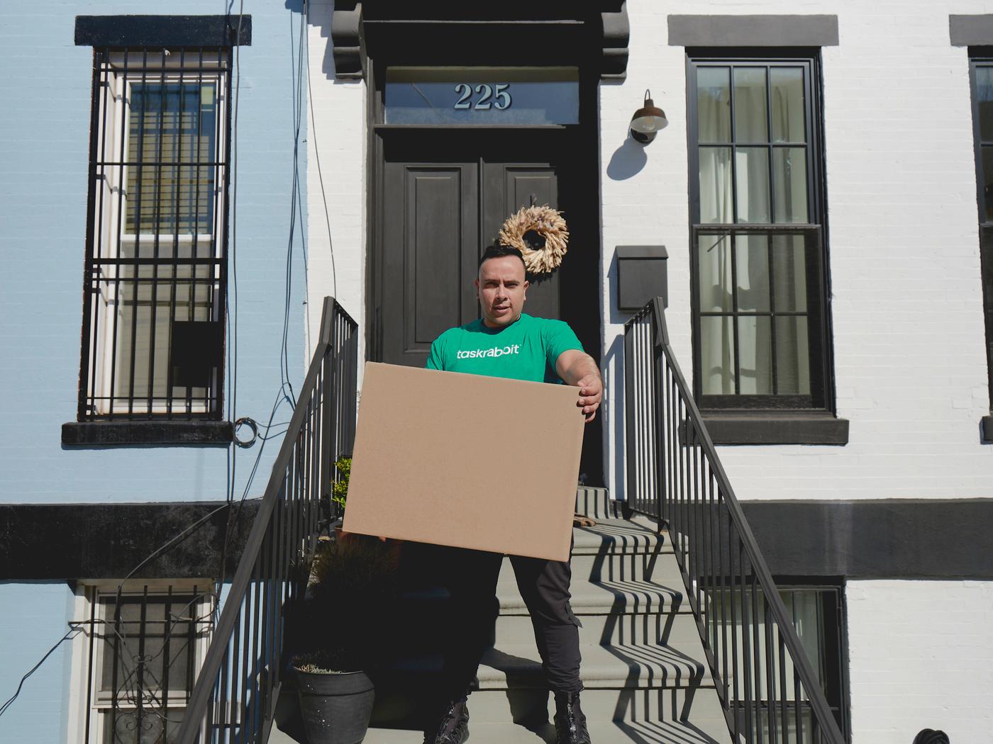 A Task Rabbit tasker stepping down the entrance stairs of a house, while holding a moving box.