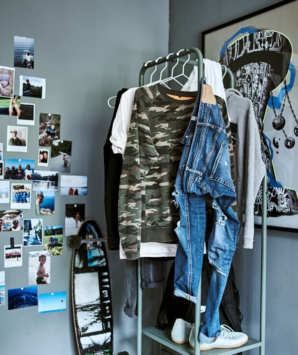 A teen room with gray walls, industrial style clothes storage, graffiti artwork and a skateboard leaning on the wall.