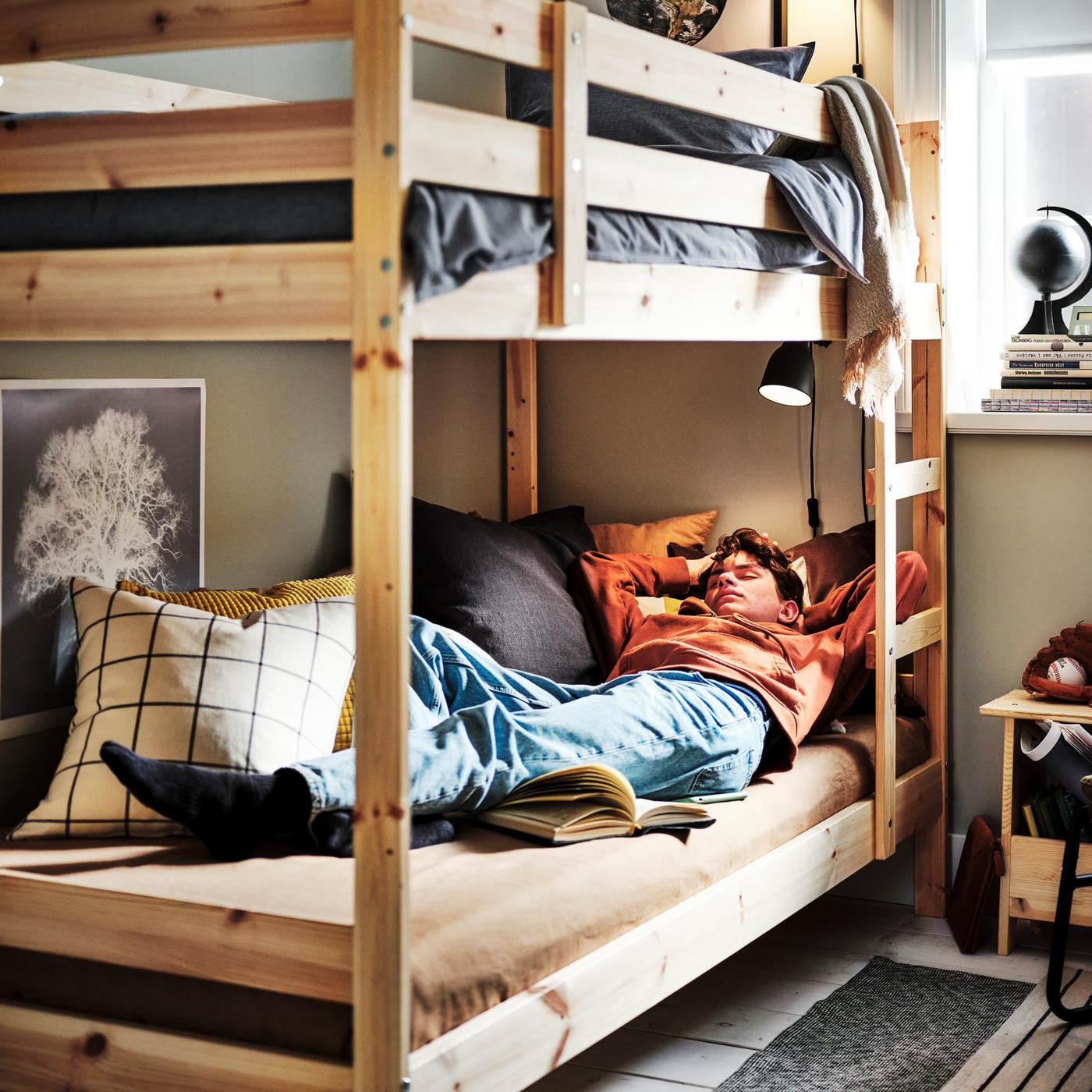 A teenager asleep on a pine MYDAL bunk bed with the top bunk dressed in a dark blue KOPPARBLAD duvet cover and pillowcase.
