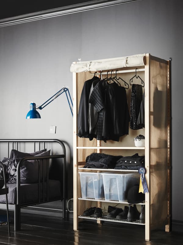 A textile sheath turns an IVAR shelving unit standing in a minimalistic, grey room, into a wardrobe, filled with clothing.