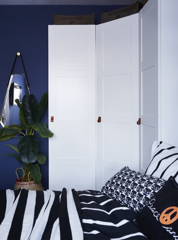 A three-door white wardrobe that wraps around a corner to conserve space in a small children's bedroom.