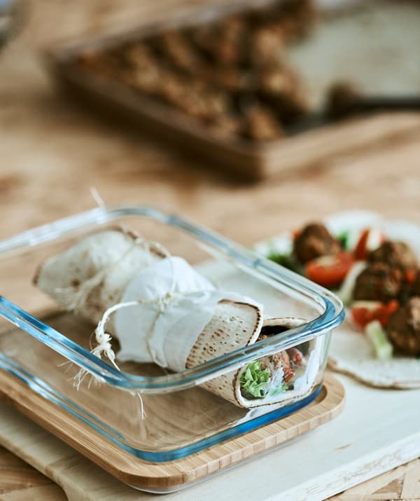 A tied tortilla veggie wrap in a glass container next to an open tortilla with filling ingredients.