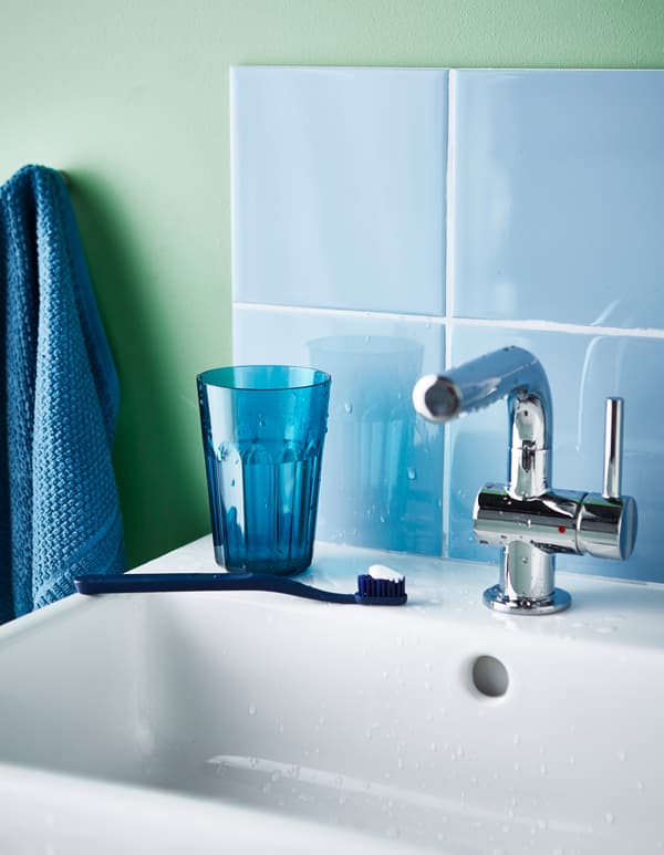 A toothbrush and small plastic mug sit on a bathroom sink.