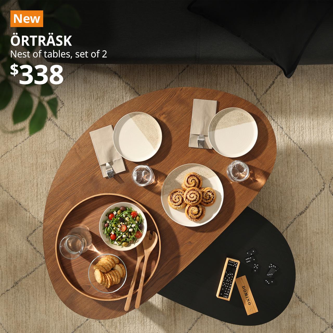A top view shot of  brown/black ash veneer ÖRTRÄSK nest of tables placed on the rug in a living room setting. An orange "NEW" label is displayed in the top left corner of the image, featuring white text that reads: "ÖRTRÄSK, Nest of tables, set of 2, $338"