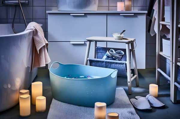 A TORKIS laundry basket being used as a footbath, surrounded by LED candles, in a bathroom.