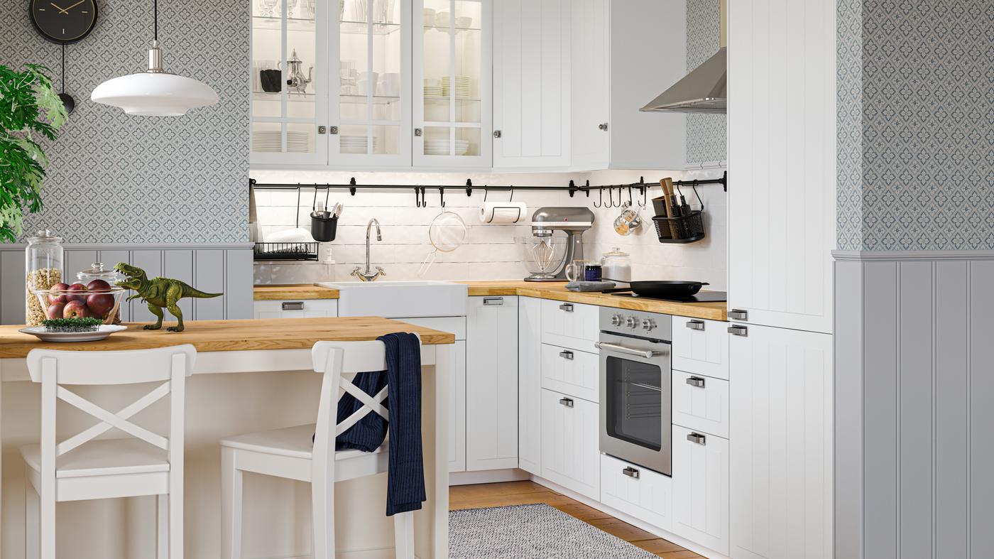 A traditional-style white STENSUND kitchen with wooden floors, floral wallpaper, and a kitchen island and two bar stools.