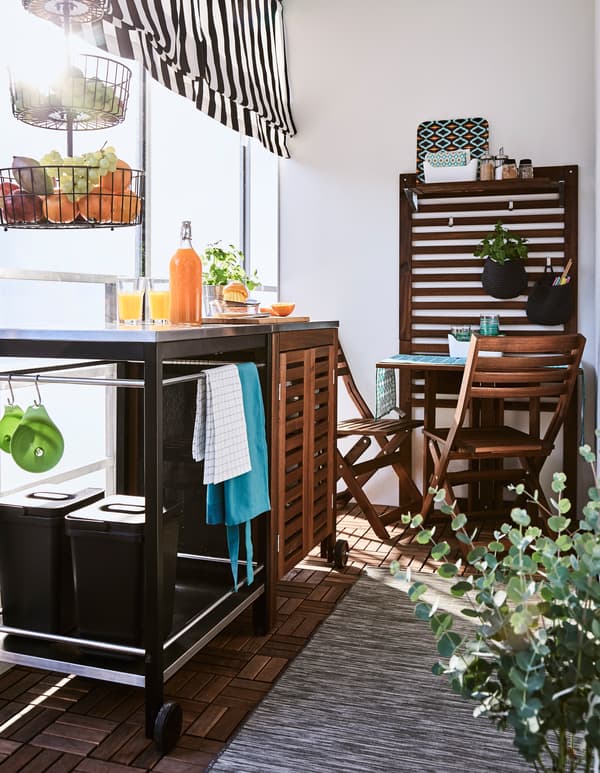 A trolley, cabinet and small table create a space to prepare and enjoy food on a balcony.