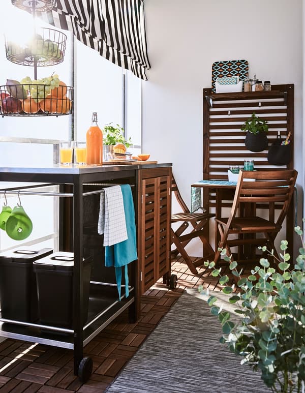 A trolley, cabinet, and small table create a space to prepare and enjoy food on a balcony.