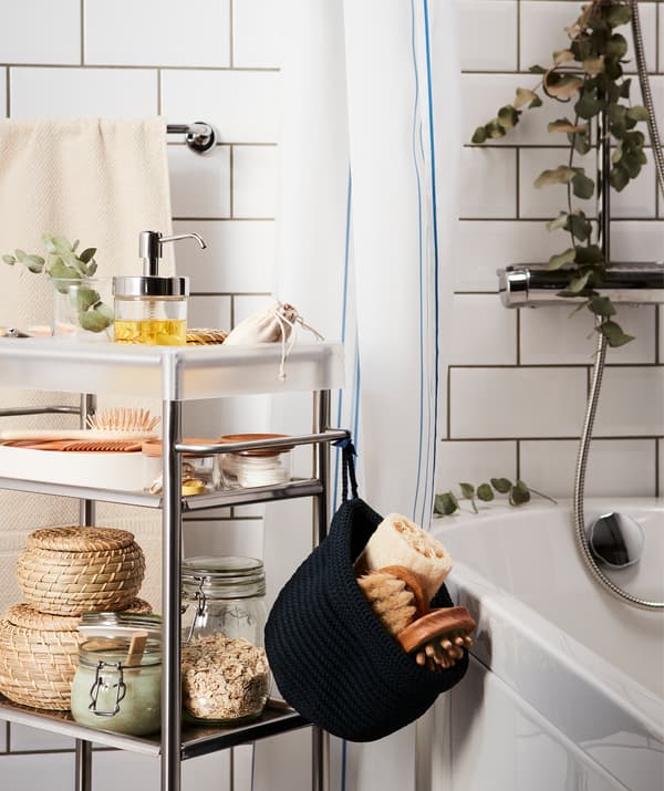 A trolley loaded with spa-style accessories, rolled in place next to a bathtub; a eucalyptus twig hangs from the shower head.