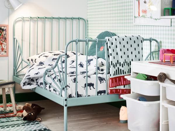A turquoise MINNEN extendable bed in the corner of a children’s room, lined with toys, reading light and storage.
