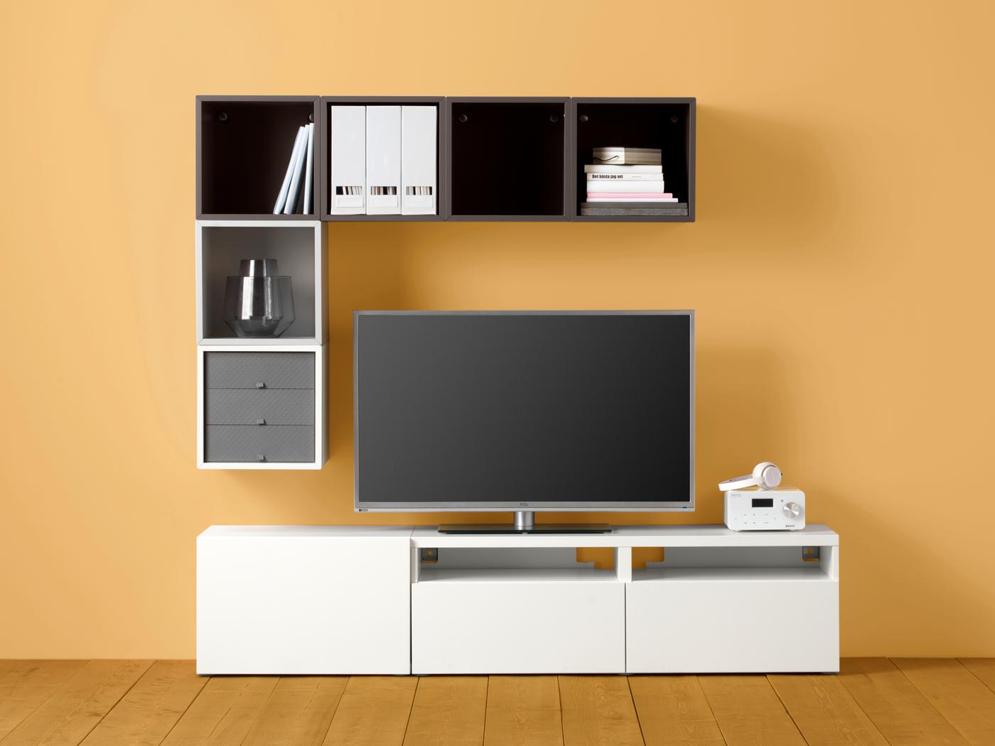 A TV framed top, side and bottom by a geometric but asymmetric combination of BESTÅ and EKET cabinets against a yellow wall.