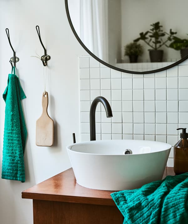 A unique washstand combines a round white modern sink with a vintage desk, next to metro tiles and a black round mirror.