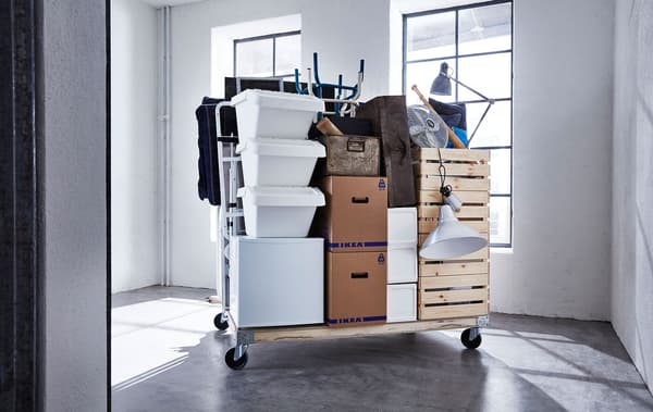 A variety of moving supplies and JÄTTENE boxes stacked on a wooden pallet with wheels, in an empty room.