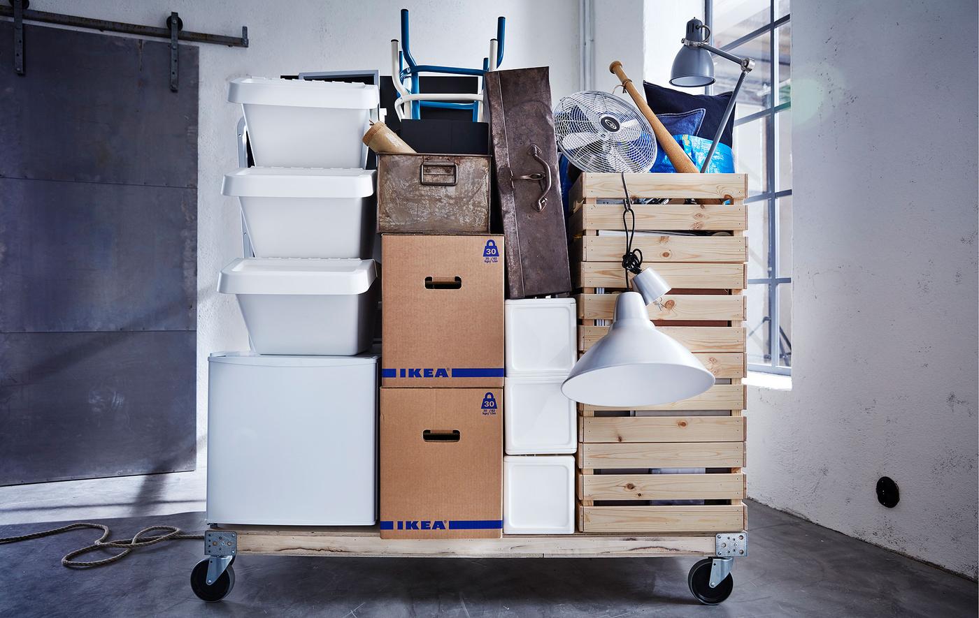 A variety of moving supplies and JÄTTENE boxes stacked on a wooden pallet with wheels, in an empty room.