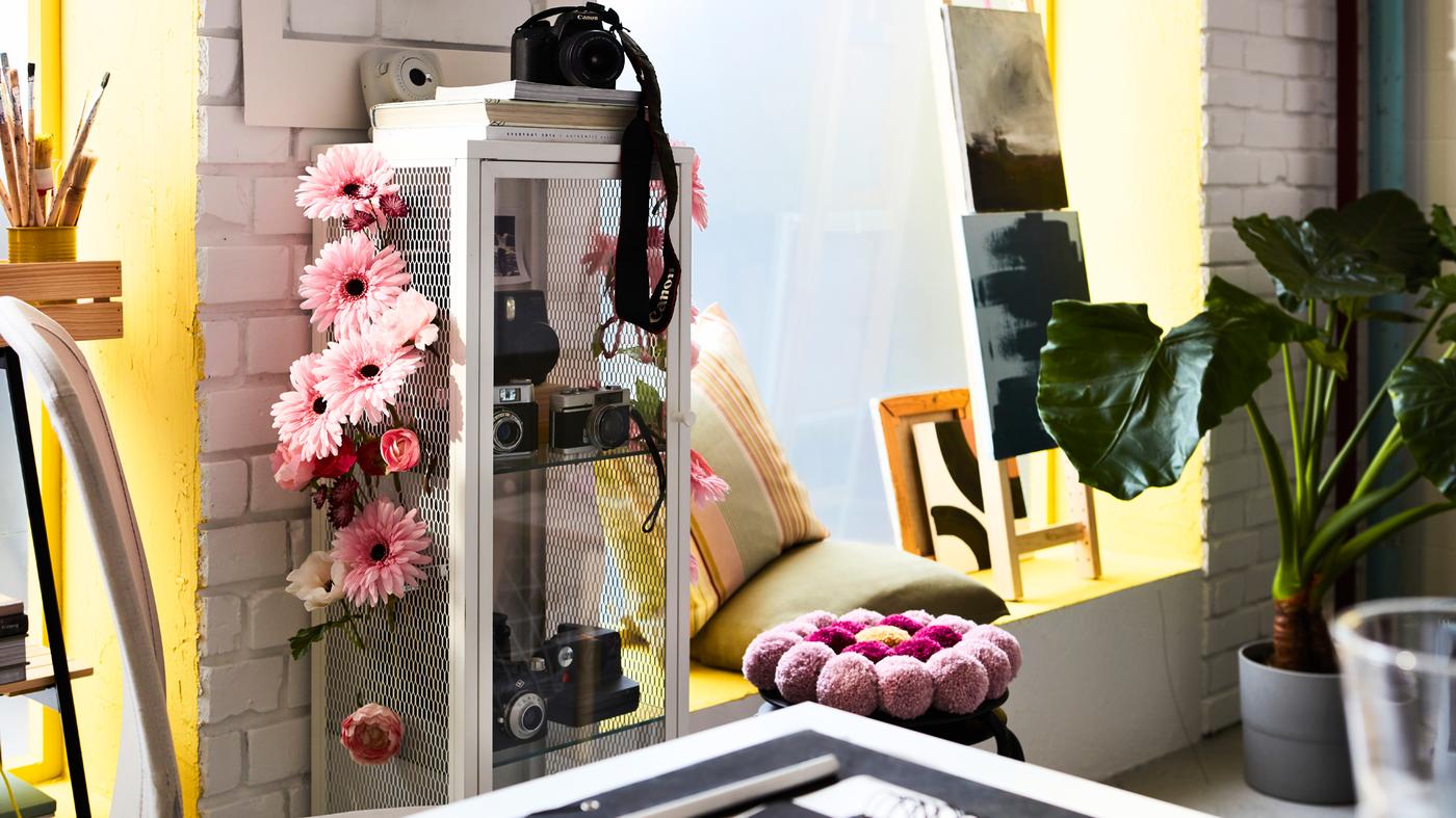 A vibrant home workspace with a BAGGEBO cabinet with glass doors customised with SMYCKA artificial flowers.