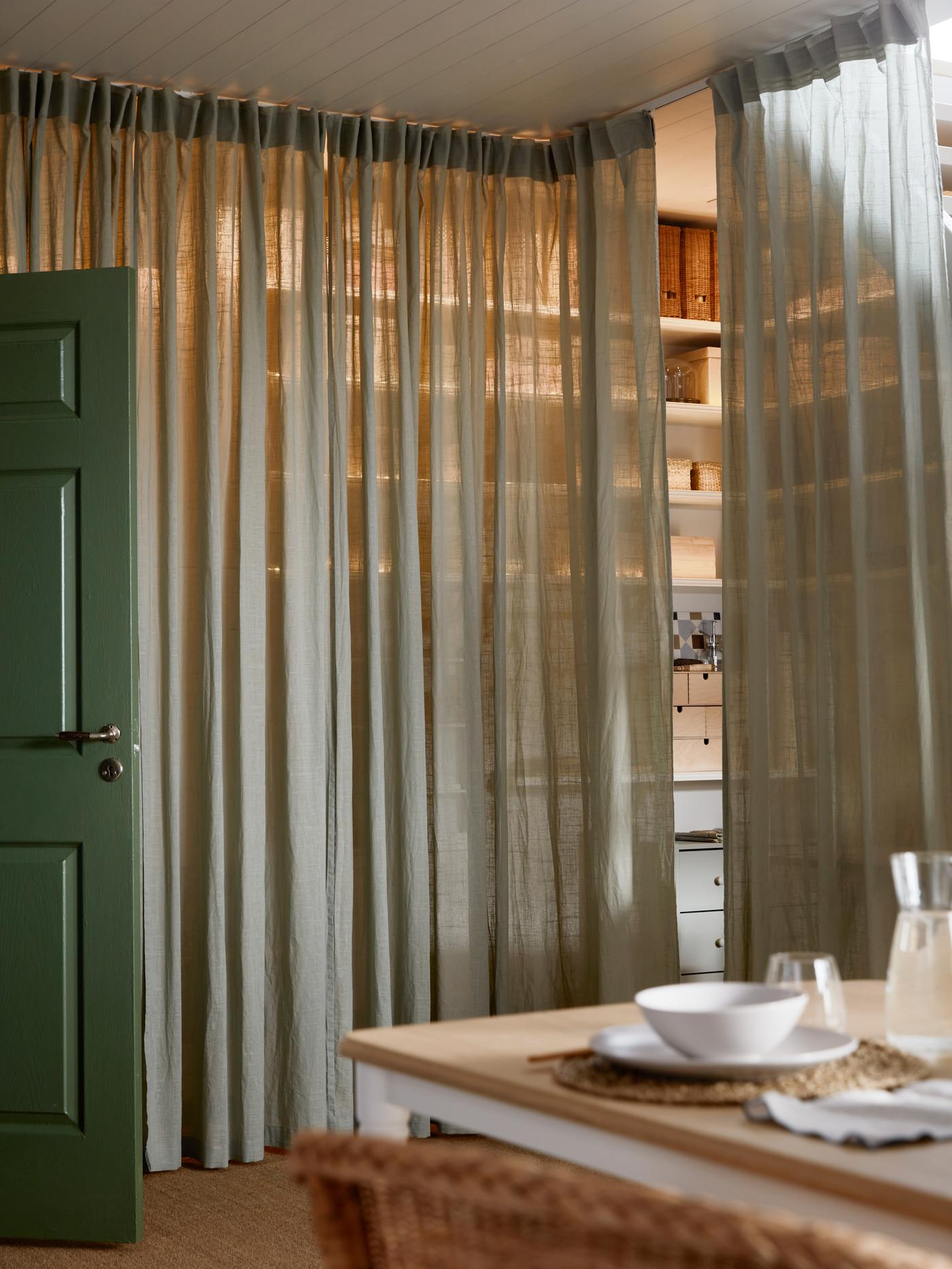 A VIDGA single track rail with a pair of light green SILVERLÖNN sheer curtains being used to conceal a wall of shelving.