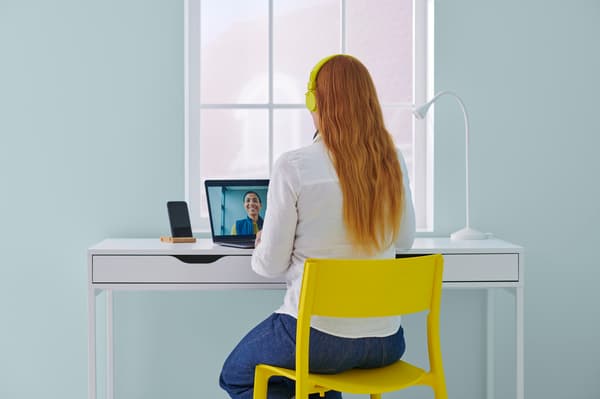 A view of a person from behind. She is sitting on a yellow chair and is on a video call.