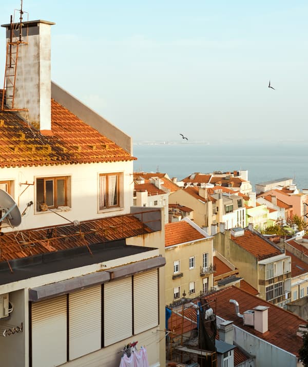 A view over red-tiled rooftops in a seaside town that leads to the water.