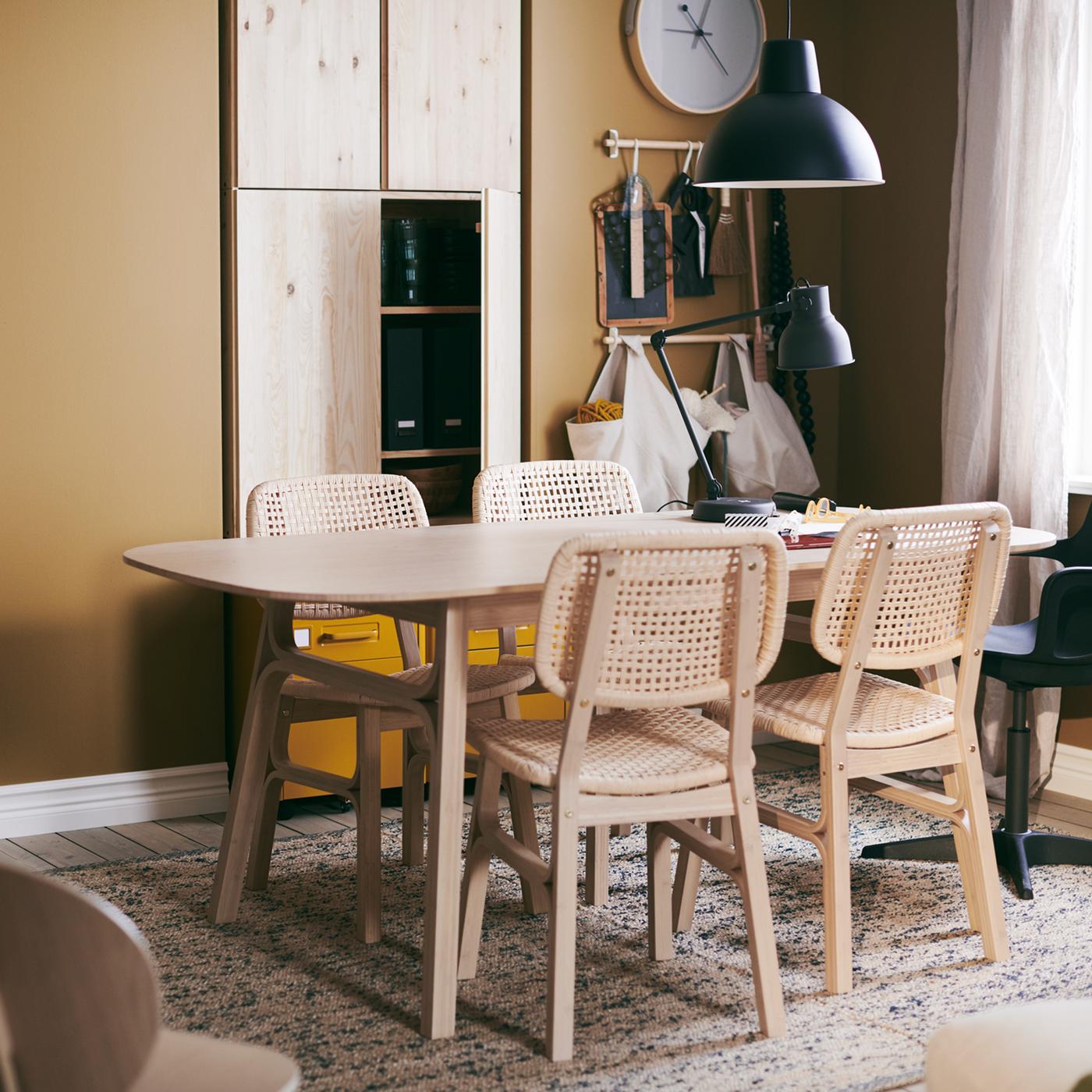 A VOXLÖV table with four chairs, standing on a MELHOLT flatwoven rug, a ROTBLÖTA wall clock on the wall and a hanging lamp.