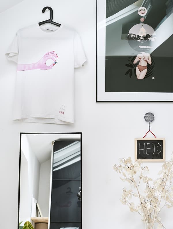 A wall decorated with a mirror, framed picture and a t-shirt on a coat hanger.