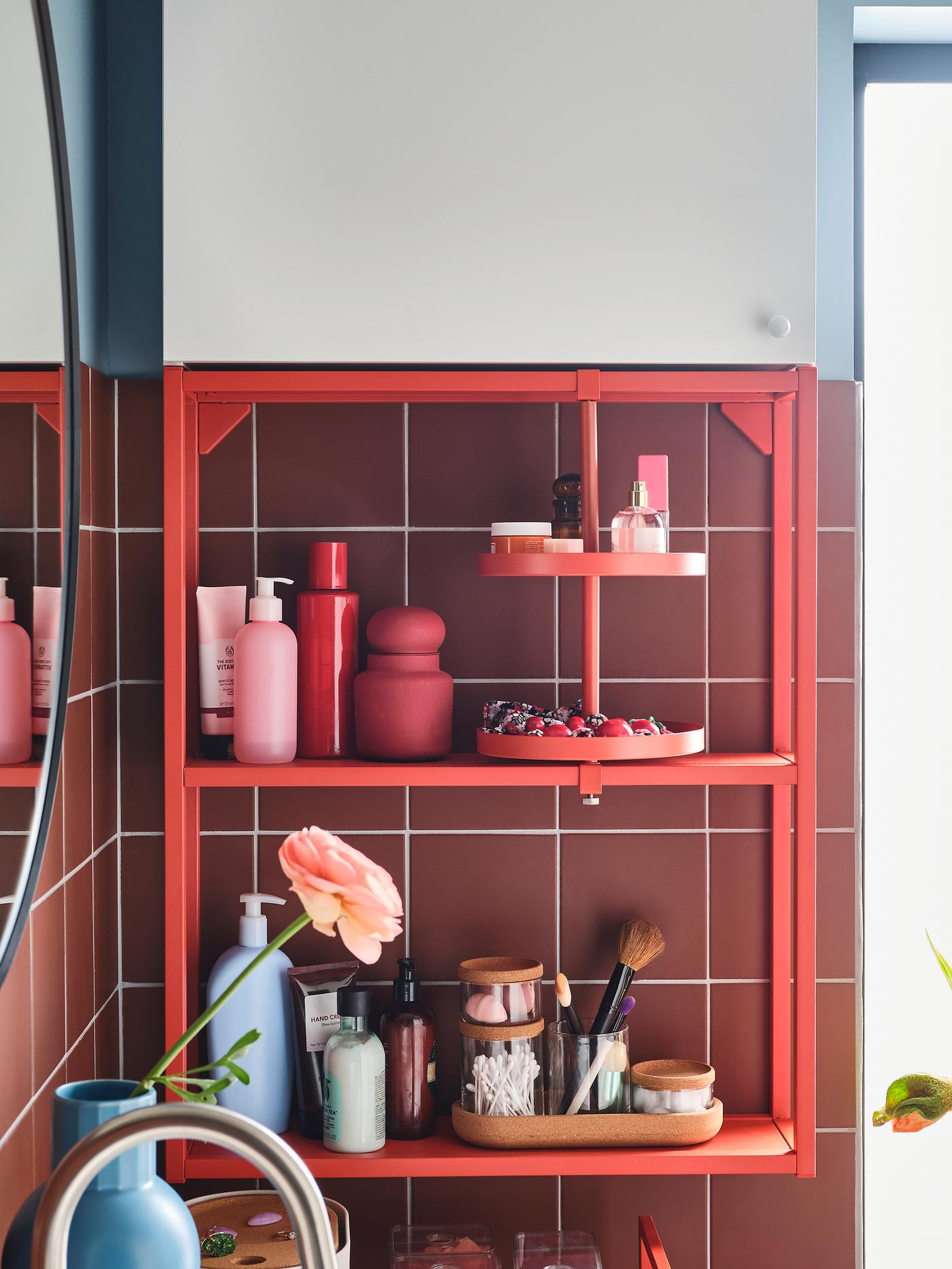 A wall frame with two shelves and a swivel shelf in red-orange, a white wall cabinet, a round mirror and a blue vase.