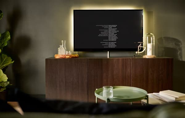 A wall-mounted TV screen has a lighting strip behind it to soften the contrast in a dark room.