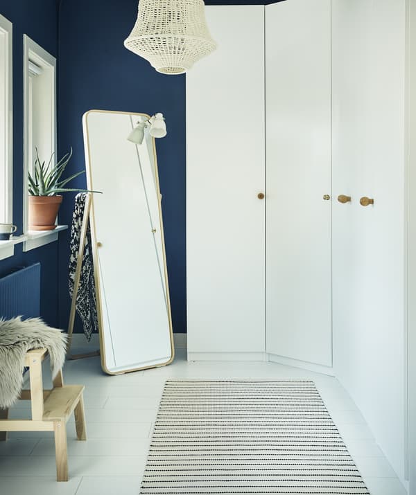 A wall of white wardrobes and a mirror in a dark blue room.