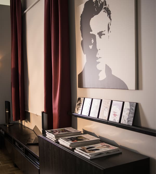 A wall with a projector screen, artwork and a picture ledge holding films.