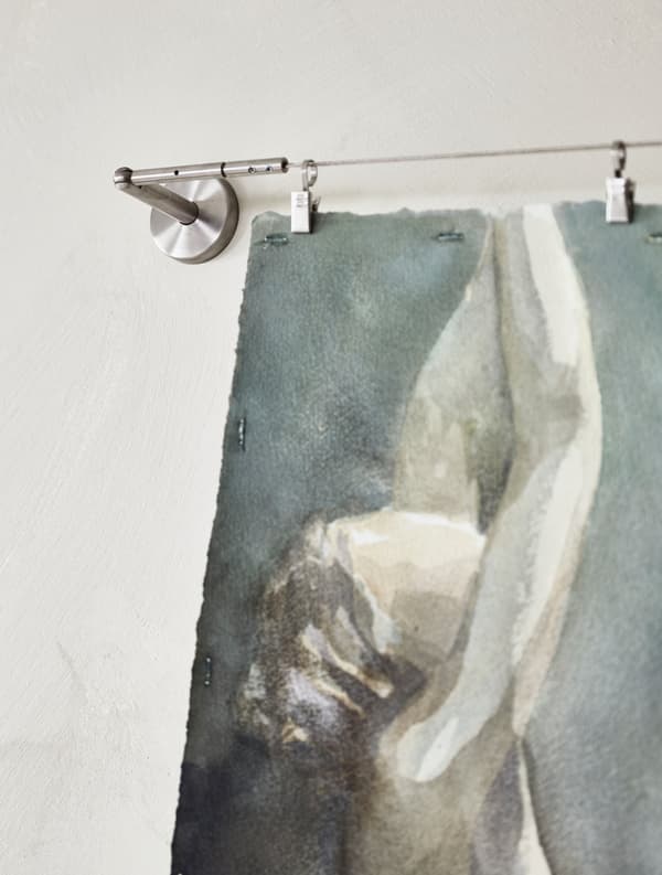 A water colour painting is hung to dry from a wire curtain hanger.
