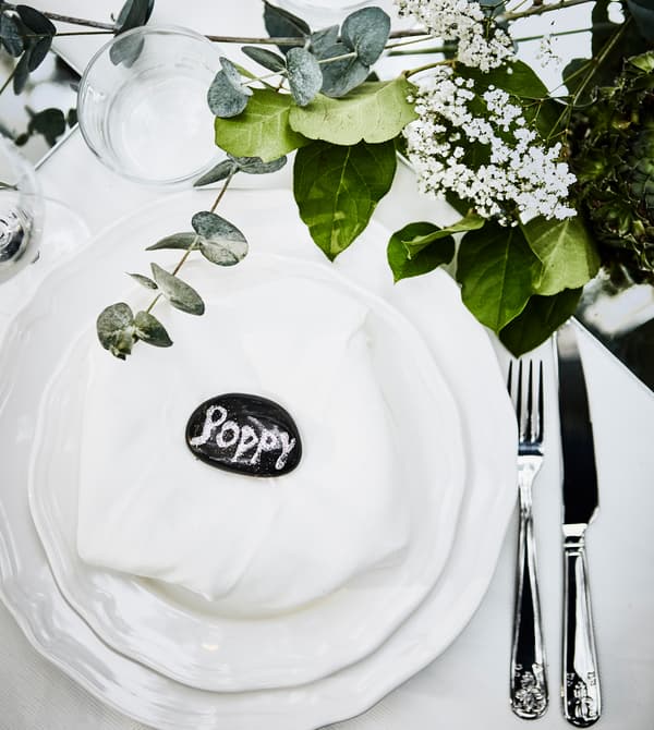 A wedding place setting with white tableware, a white napkin and a glittery painted rock as a name tag