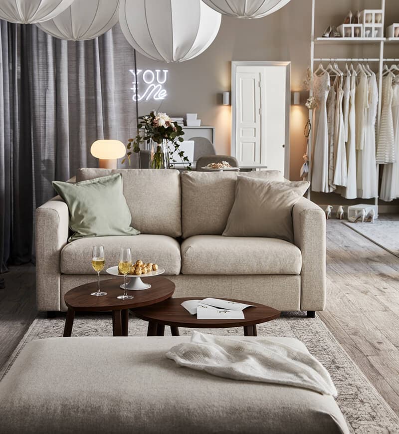 A wedding planner office featuring a light beige room setting with a light beige sofa, dark brown coffee table and an assortment of wedding dresses at the back of the room.