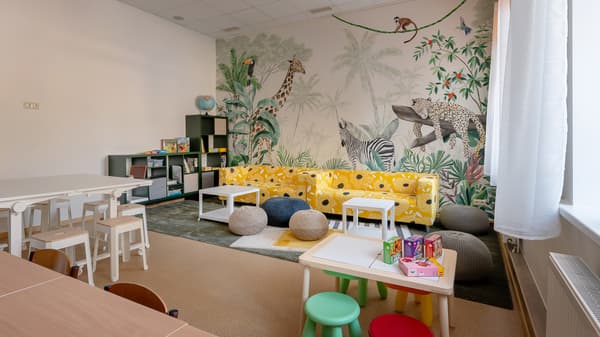 A welcoming after-school space with study tables, a lounge area, and a tropical jungle mural featuring animals such as a giraffe, zebra, and leopard. Bright yellow sofas, soft seating, and playful details create a cosy and cheerful environment for learning, relaxation, and socialising.