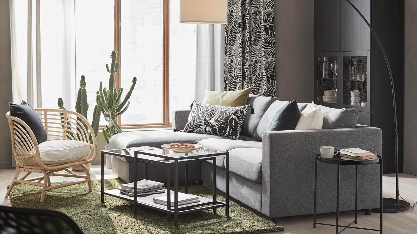 A well-lit modern living room with a gray sofa, rattan chair, cactus, and a two-tier coffee table.