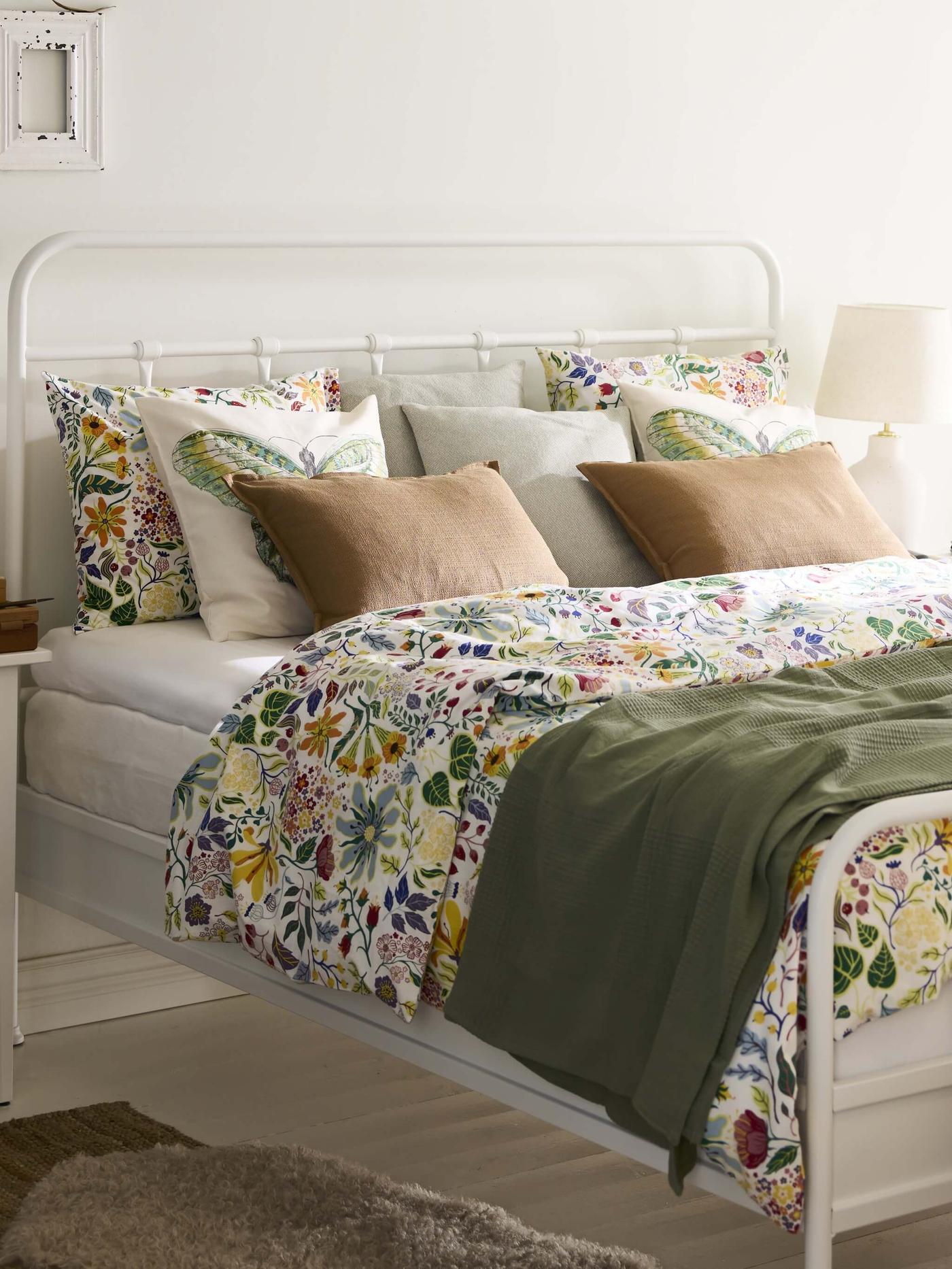 A well-made bed with colorful floral bedding and tan pillows in a bright room.